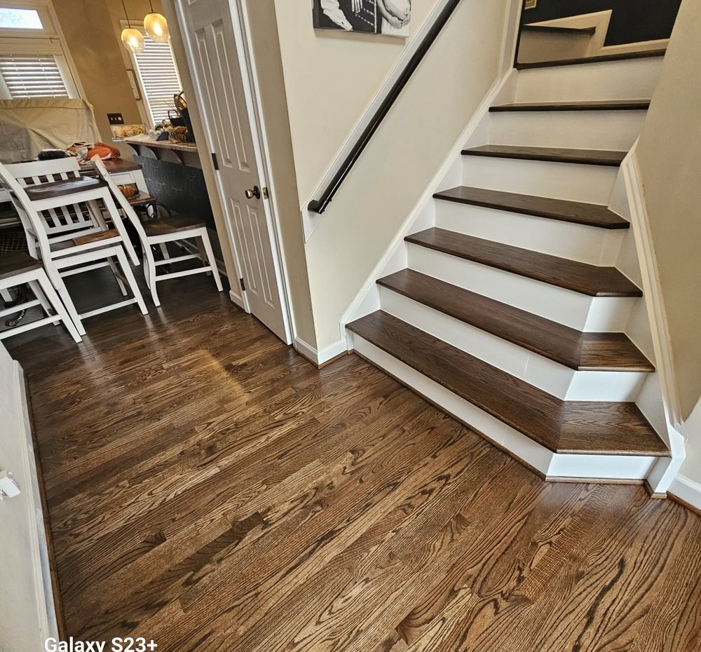 Dark stained oak stair treads with white risers meeting a refinished red oak floor